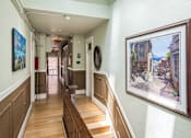 Thumbnail 6 of 12 - A hallway with a staircase and a painting on the wall.
