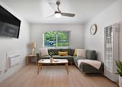 Thumbnail 3 of 16 - A living room with a grey couch, a wooden table, and a ceiling fan.
