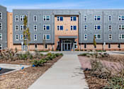 Thumbnail 37 of 42 - A modern building with a grey and orange facade and a walkway leading to the entrance.