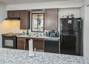Thumbnail 8 of 14 - A kitchen with a black fridge, white countertop, and brown cabinets.