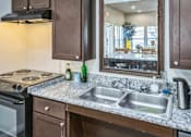 Thumbnail 9 of 14 - A kitchen with a stove, sink, and a mirror reflecting a dining area.