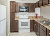 Thumbnail 10 of 14 - A kitchen with brown cabinets and a white stove top oven.