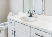 Thumbnail 5 of 13 - A white bathroom with a sink, mirror, and toilet.