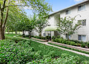 Thumbnail 27 of 32 - A white building with a green awning is surrounded by trees and bushes.
