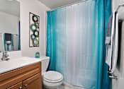 Thumbnail 23 of 32 - A bathroom with a white sink, a toilet, a blue shower curtain, and a mirror.