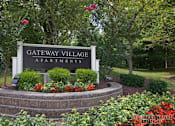 Thumbnail 13 of 13 - A sign for Gateway Village Apartments is surrounded by flowers and greenery.