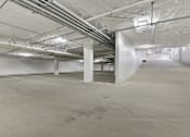 Thumbnail 16 of 18 - A large, empty, industrial-style room with concrete floors and exposed pipes and ducts.