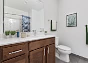 Thumbnail 7 of 18 - A bathroom with a white toilet, a sink with a mirror above it, and a plant on the counter.