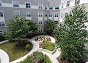 Thumbnail 1 of 4 - A courtyard with a circular garden and a building in the background.