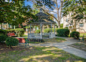Thumbnail 3 of 18 - A gazebo is surrounded by green bushes and trees.