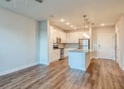 Thumbnail 2 of 42 - an empty living room with a kitchen with white cabinets at The Bella at Westchester, Virginia