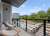 Thumbnail 8 of 25 - A balcony with a chair and table overlooking a pool and trees.