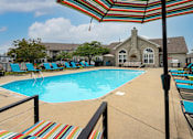 Thumbnail 12 of 21 - A pool with a striped umbrella and chairs.