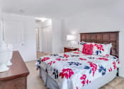 Thumbnail 6 of 17 - A bed with a floral print is in the center of a bedroom with a wooden dresser and a white vase on top.