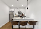 Thumbnail 14 of 51 - A kitchen with a refrigerator, microwave, and two chairs.