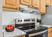 Thumbnail 1 of 14 - A kitchen with a stove, refrigerator, and a bowl of apples on the counter.