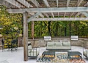 Thumbnail 57 of 67 - A wooden pergola with a couch and chairs underneath it.