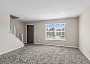 Thumbnail 36 of 54 - A spacious room with a carpeted floor, a staircase, and a large window overlooking a parking lot.
