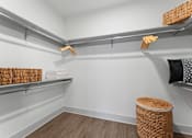 Thumbnail 13 of 25 - A room with a white wall and a shelf with baskets and towels.