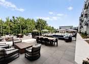 Thumbnail 18 of 25 - A patio with black chairs and tables is surrounded by trees.