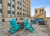 Thumbnail 36 of 46 - a patio with blue chairs and a fire pit in front of a brick building