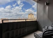Thumbnail 41 of 52 - A balcony with a chair and a table with a view of a building in the distance.