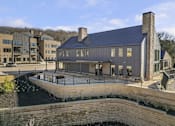 Thumbnail 38 of 51 - A modern building with a black roof and a stone wall in front.