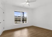 Thumbnail 5 of 44 - A room with a ceiling fan and a large window overlooking a parking lot.