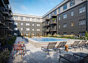 Thumbnail 3 of 27 - A pool surrounded by lounge chairs and buildings.