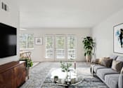 Thumbnail 5 of 14 - A modern living room with a grey sofa, a coffee table, and a flat-screen TV.