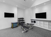 Thumbnail 16 of 50 - A black and yellow box sits on a grey carpet in a room with a row of dumbbells in the background.