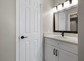 Thumbnail 19 of 67 - A white bathroom with a door, sink, and mirror.