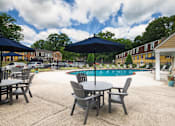 Thumbnail 23 of 39 - A pool area with a table and chairs and umbrellas.