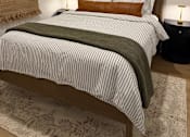 Thumbnail 17 of 29 - A bed with a striped comforter and a brown pillow is in the image.