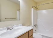 Thumbnail 19 of 26 - A white sink with a mirror above it and a white bathtub with a shower curtain.