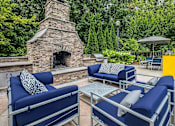 Thumbnail 12 of 20 - A patio with blue couches and a stone fireplace.