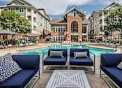 Thumbnail 8 of 20 - A pool area with blue couches and a brick building in the background.