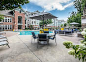 Thumbnail 11 of 20 - A pool area with chairs and umbrellas in front of a building.