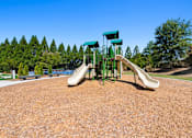 Thumbnail 8 of 34 - A playground with a green slide and a brown surface.