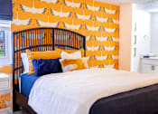 Thumbnail 21 of 31 - A bed with a white comforter and a blue pillow is in front of a wallpapered wall.
