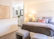 Thumbnail 18 of 31 - A bedroom with a large bed and a grey ottoman.