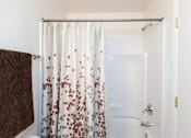 Thumbnail 17 of 22 - A white shower curtain with red and grey flowers is hanging in a white bathroom.