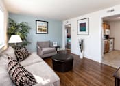 Thumbnail 2 of 19 - A living room with a grey couch, a round ottoman, and a potted plant.