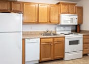 Thumbnail 6 of 19 - A white refrigerator stands next to a white dishwasher in a kitchen with wooden cabinets.