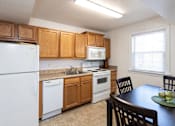 Thumbnail 5 of 19 - A kitchen with a white refrigerator, brown cabinets, and a black table.