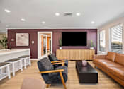 Thumbnail 3 of 29 - A living room with a grey armchair, a brown leather sofa, a wooden coffee table, and a white bench with black cushions.