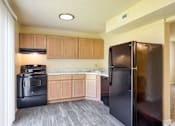 Thumbnail 26 of 26 - A black refrigerator is in a kitchen with wooden cabinets.