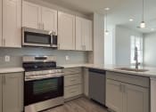 Thumbnail 36 of 47 - an empty kitchen with white cabinets and stainless steel appliances at The Port at East Beach Apartments and Marina, Norkfolk, VA