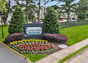 Thumbnail 53 of 56 - A sign for Latitudes Capayment surrounded by greenery and flowers.