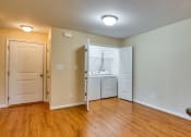 Thumbnail 8 of 21 - an empty living room with wood flooring and a kitchen with white appliances